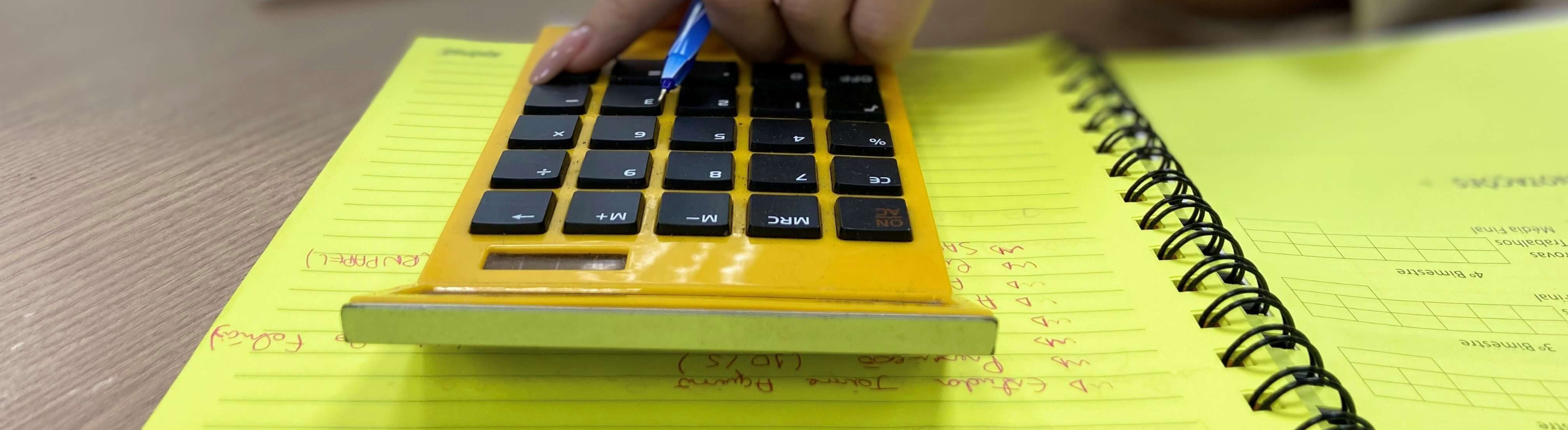 Imagem mostra mão feminina utilizando uma calculadora amarela