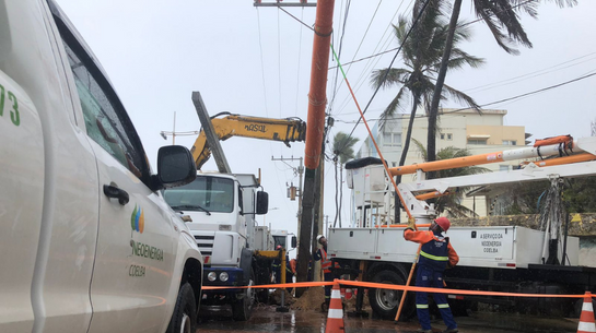 Foto de poste sendo instalado com caminhões ao redor