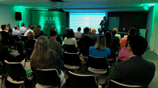 Foto de plateia assistindo ao seminário com tela escrito SAMP e apresentação