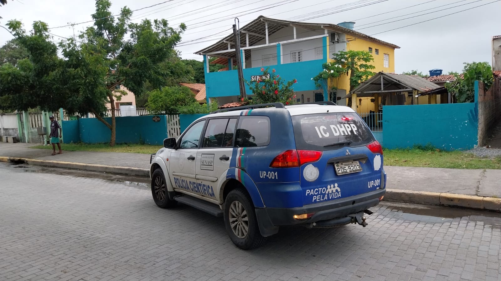Carro da polícia estacionamento enfrente a uma casa de muro azul.