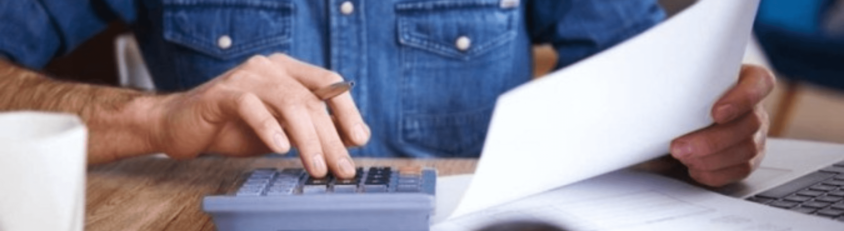 Mãos de um homem segurando uma caneta e um papel sobre uma calculadora