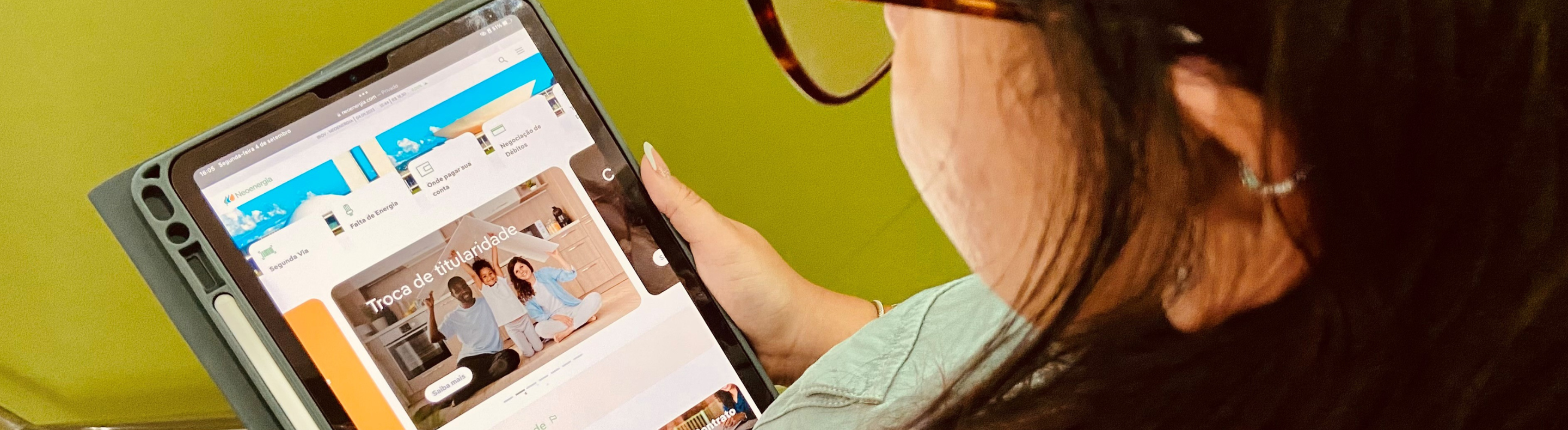 Cliente da Neoenergia Pernambuco com tablet na homepage do site da Neoenergia em mãos