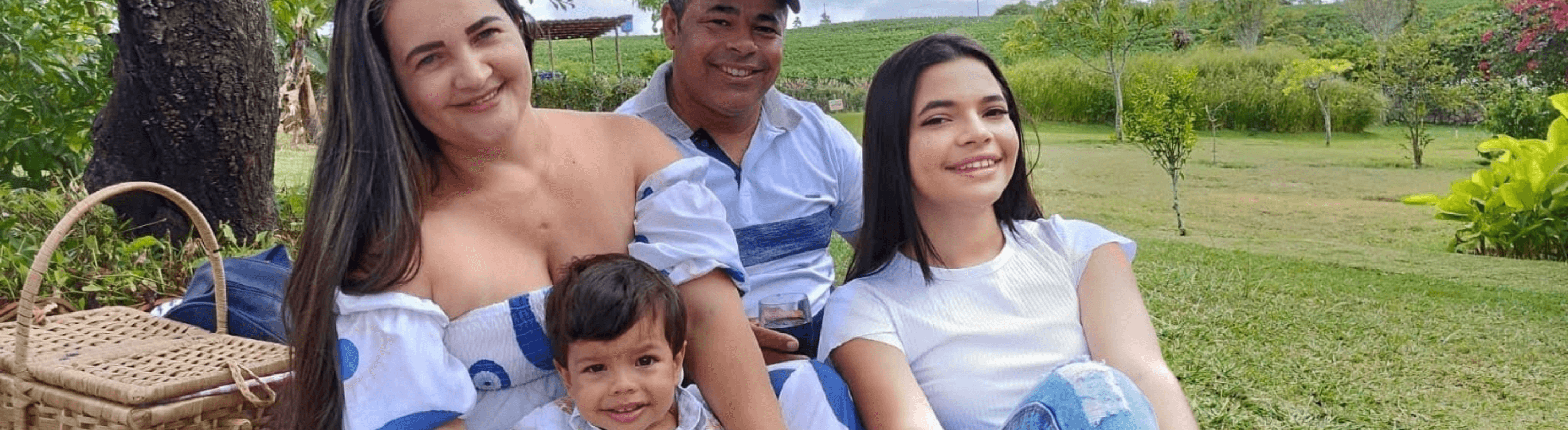 Uma mulher adulta, um homem adulto, uma crianla de colo e uma adolescente em um piquenique no campo