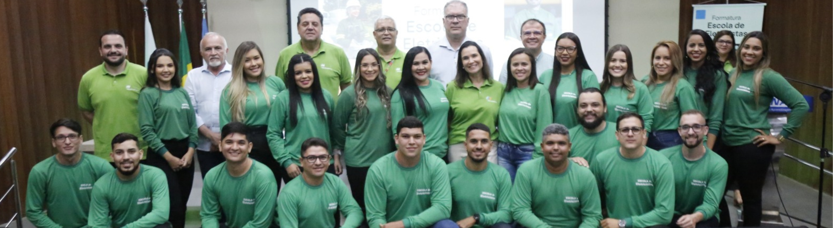 Imagem mostra homens e mulheres em pé a agachados após cerimônia de formatura da Escola de Eletricistas da Neoenergia