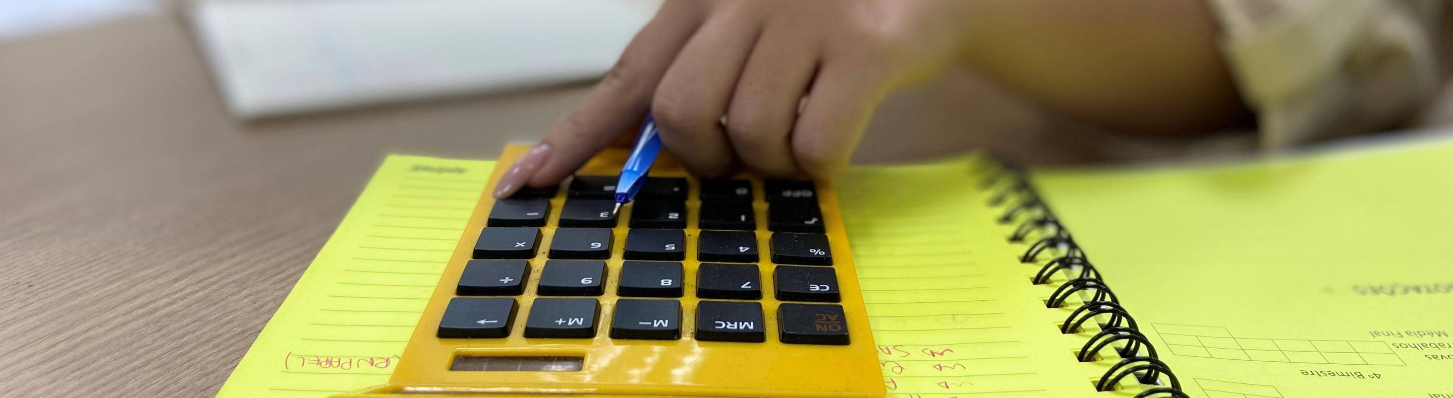 Imagem mostra uma pessoa com unhas pintadas utilizando uma calculadora amarela