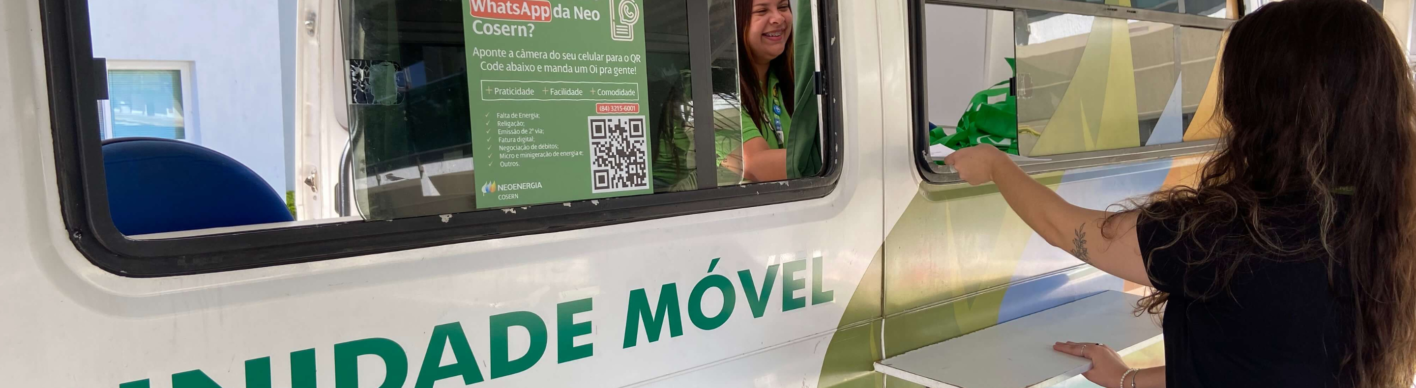 Imagem mostra pessoa de cabelo longo e escuro sendo atendida na Unidade Móvel da Neoenergia Cosern por uma atendente mulher
