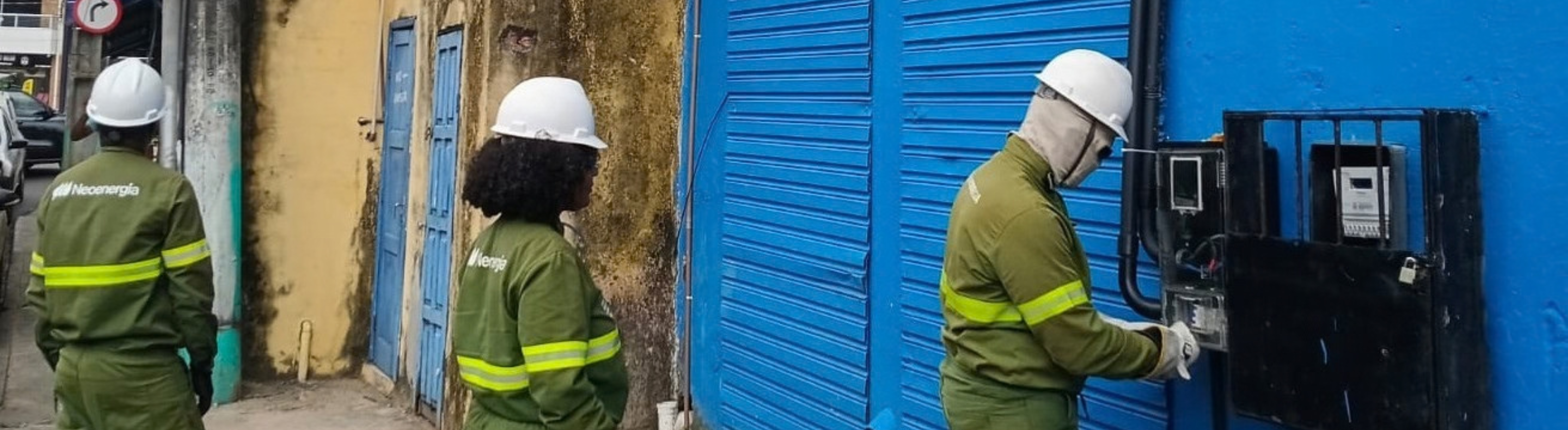 Técnicos da Neoenergia Coelba mexem em medidor de energia com sinais de adulteração. Operação ocorre durante inspeções para combate a fraudes de energia. Técnicos estão fardados e de costas para a câmera, evitando identificação.
