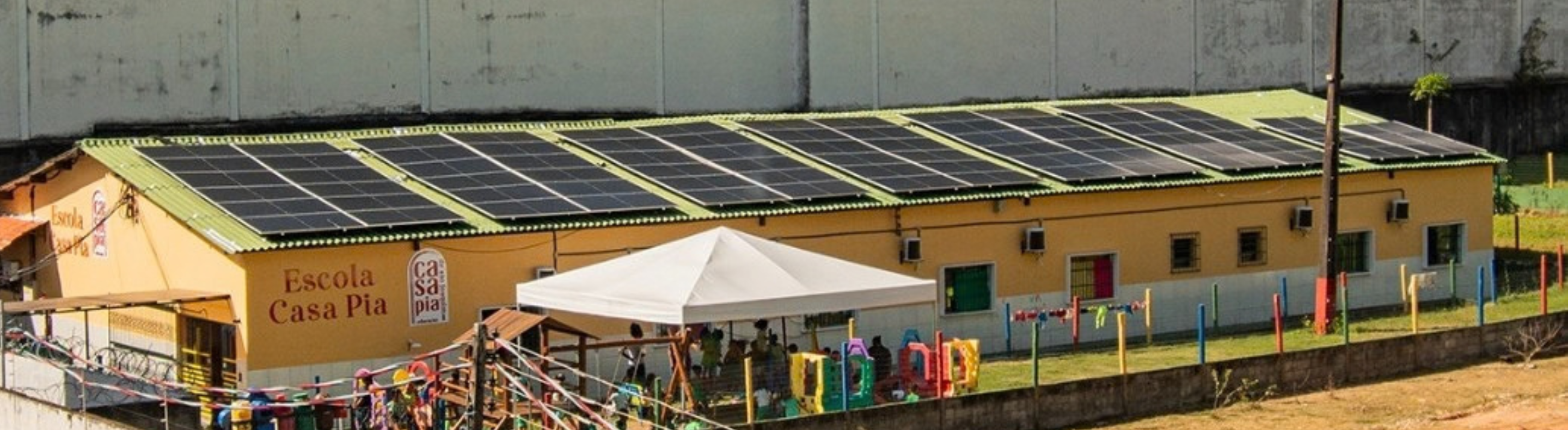 Imagem apresenta visão aérea do telhado da Escola Casa Pia - centro educativo do projeto filantrópico Casa Pia. A cobertura da escola possui um sistema de geração fotovoltaicas, com placas solares que cobrem todo o espaço.