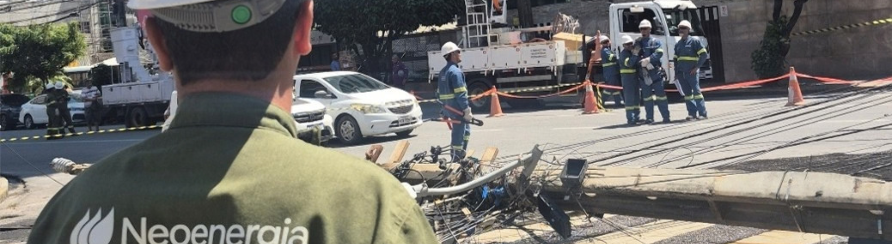 Colaboradores da Neoenergia atuam em ocorrência de queda de poste após colisão de veículo. Profissional está em pé olhando para estrutura (poste) lançado ao chão