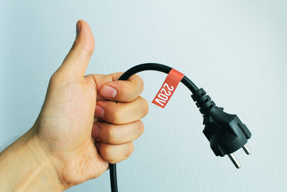 Mão segurando um plugue de 220V com etiqueta de identificação