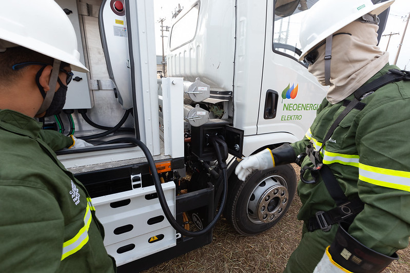 duas pessoas com EPI abastecendo caminhão elétrico