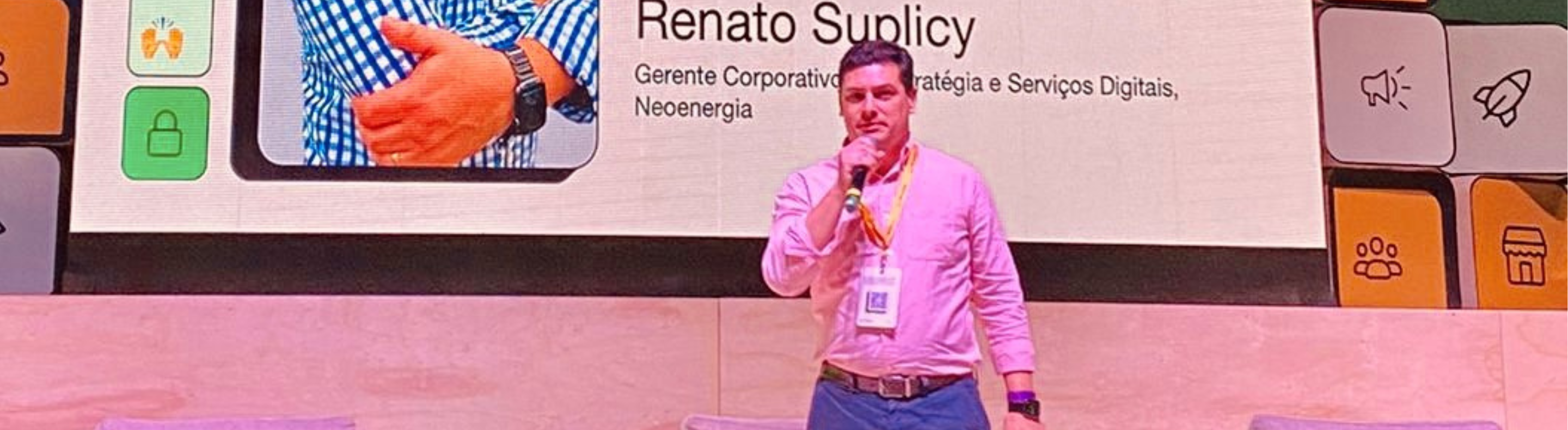 Imagem mostra Renato Suplicy, gerente corporativo de Estratégia e Serviços Digitais, vestindo camisa rosa e segurando microfone durante palestra