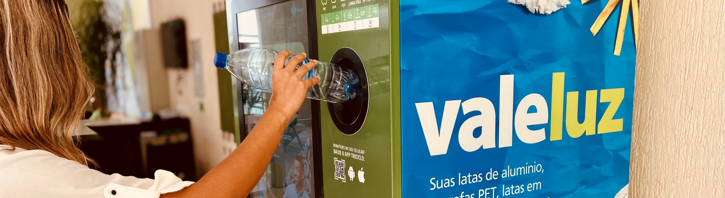 Imagem mostra mulher depositando uma garrafa plástica em uma máquina de reciclagem do projeto Vale Luz, da Neoenergia