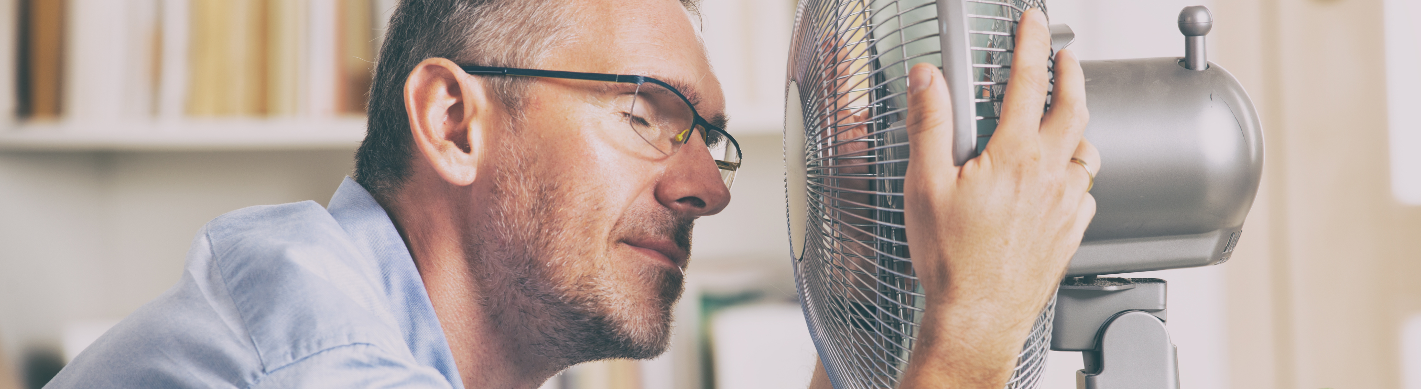 Imagem mostra homem se refrescando do calor em frente a um ventilador