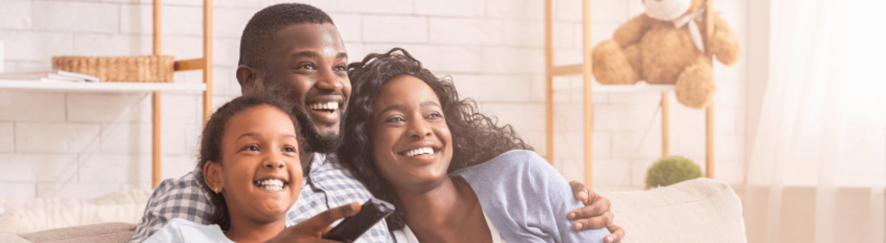 Um homem, uma mulher e uma criança de pele negra sorrindo sentados em um sofá